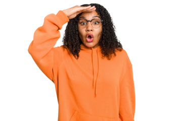 Young african american woman with curly hair cut out isolated looking far away keeping hand on forehead.