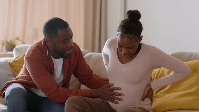 Beginning of labor. Young pregnant african american woman feeling sudden contractions, worried husband calling to doctor