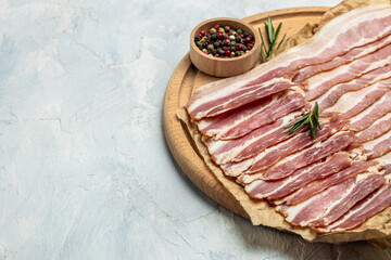 Portion of raw Bacon stripes with rosemary on a wooden board on a light background, ketogenic diet, place for text, top view