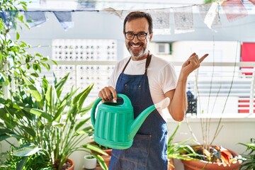 Middle age man wearing gardener apron holding watering can at home terrace smiling happy pointing with hand and finger to the side © Krakenimages.com