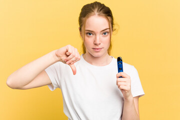 Young cute woman holding a vaper isolated on yellow background showing a dislike gesture, thumbs...