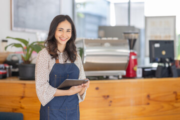 Portrait young Asian woman barista feeling happy smiling at urban cafe. Small business owner Asian girl in apron at small business entrance.