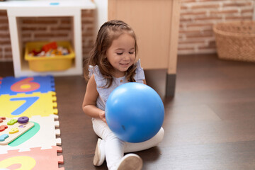 Adorable hispanic girl playing with ball sitting on floor at kindergarten