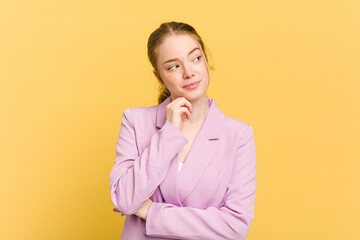 Young caucasian redhead woman isolated on yellow background thinking and looking up, being reflective, contemplating, having a fantasy.