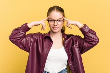 Young caucasian redhead woman isolated on yellow background focused on a task, keeping forefingers pointing head.