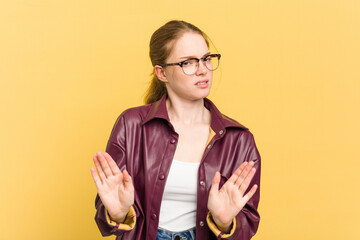 Young caucasian redhead woman isolated on yellow background rejecting someone showing a gesture of...
