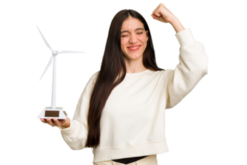 Young caucasian woman holding a small wind energy mill isolated raising fist after a victory, winner concept.