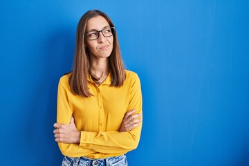 Obraz premium Young woman wearing glasses standing over blue background smiling looking to the side and staring away thinking.