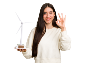 Young caucasian woman holding a small wind energy mill isolated cheerful and confident showing ok gesture.