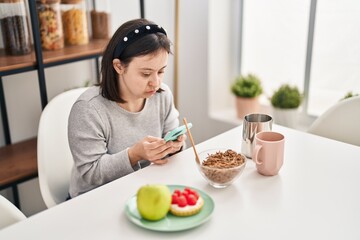 Young woman with down syndrome using smartphone having breakfast at home