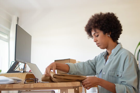 Serious Blackwoman Folding Garment For Dispatch. Concentrated African American Online Store Employeer Working In Office. Packing Package Concept