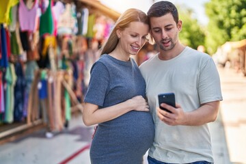 Man and woman couple expecting baby using smartphone at street market
