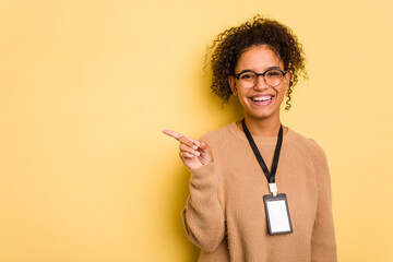 Young brazilian woman with a badge isolated on yellow background smiling and pointing aside, showing something at blank space.