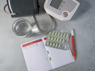 Control and measurement of blood pressure and pulse at home. Sphygmomanometer, a notebook for recording the results of measuring blood pressure, a pen, green pills, a glass of water. Hypertension