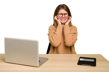Young caucasian woman in a workplace working with a laptop isolated covering ears with hands.