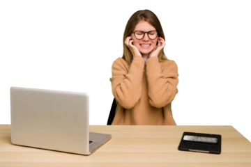 Young caucasian woman in a workplace working with a laptop isolated covering ears with hands.