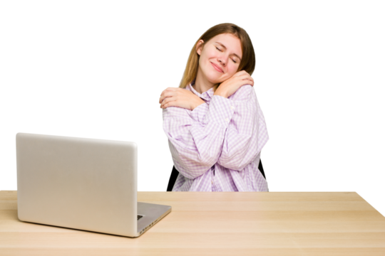 Young caucasian woman in a workplace working with a laptop isolated hugs, smiling carefree and happy.