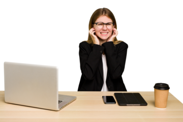 Young business caucasian woman working on her workplace cutout isolated covering ears with hands.