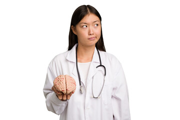 Young asian doctor woman holding a brain isolated confused, feels doubtful and unsure.