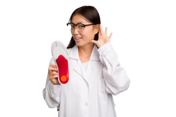 Young asian chiropodist holding a insoles for shoes isolated trying to listening a gossip.