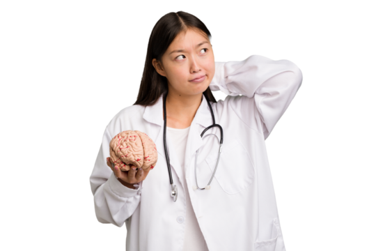 Young asian doctor woman holding a brain isolated touching back of head, thinking and making a choice.
