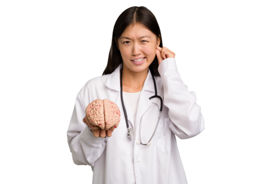 Young asian doctor woman holding a brain isolated covering ears with hands.