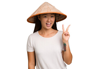 Obraz na płótnie Canvas Young asian woman wearing a Vietnamese hat isolated joyful and carefree showing a peace symbol with fingers.