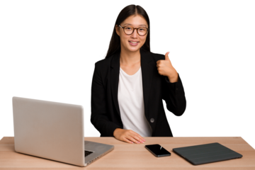 Young business asian woman sitting on a table isolated smiling and raising thumb up
