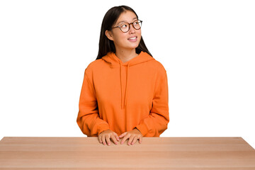 Young asian woman sitting on a table isolated relaxed and happy laughing, neck stretched showing teeth. - Powered by Adobe