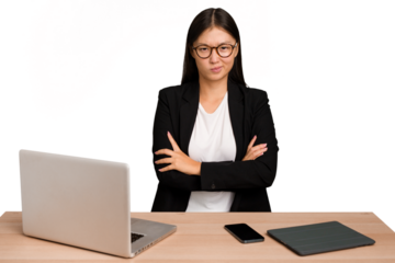 Young business asian woman sitting on a table isolated frowning face in displeasure, keeps arms folded.