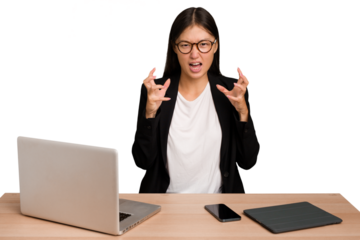 Young business asian woman sitting on a table isolated screaming with rage.