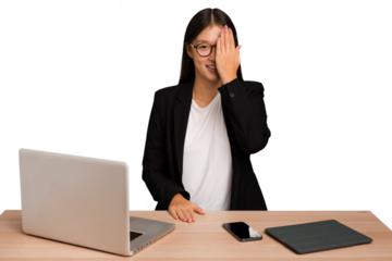 Young business asian woman sitting on a table isolated having fun covering half of face with palm.