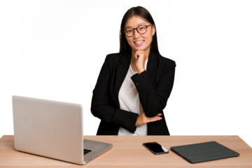 Young business asian woman sitting on a table isolated smiling happy and confident, touching chin with hand.