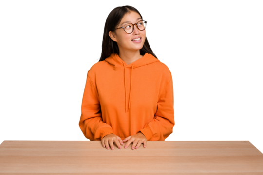 Young asian woman sitting on a table isolated relaxed and happy laughing, neck stretched showing teeth.
