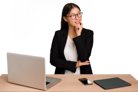 Young business asian woman sitting on a table isolated relaxed thinking about something looking at a copy space.