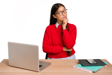 Young student asian woman in a workplace with a laptop isolated thinking and looking up, being reflective, contemplating, having a fantasy.