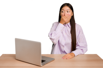 Young student asian woman in a workplace with a laptop isolated thoughtful looking to a copy space covering mouth with hand.