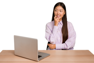 Young student asian woman in a workplace with a laptop isolated relaxed thinking about something looking at a copy space.