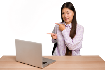 Young student asian woman in a workplace with a laptop isolated shocked pointing with index fingers to a copy space.