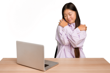 Young student asian woman in a workplace with a laptop isolated hugs, smiling carefree and happy.