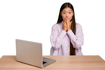 Young student asian woman in a workplace with a laptop isolated shocked, covering mouth with hands, anxious to discover something new.