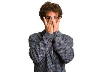Young curly smart caucasian man cut out isolated blink at the camera through fingers, embarrassed covering face.