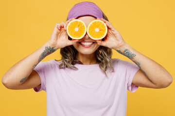 Calm young smiling woman she wears purple pyjamas jam sleep eye mask rest relax at home cover eyes with half of oranges isolated on plain yellow background studio portrait Good mood night nap concept