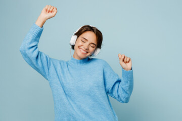 Young happy caucasian woman wear knitted sweater headphones listen to music raise up hands dance...