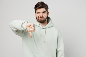 Young dissatisfied sad unhappy displeased unshaven caucasian man wear mint hoody showing thumb down...