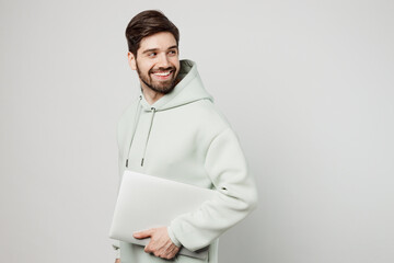 Young fun programmer happy caucasian man wear mint hoody hold closed laptop pc computer look aside on workspace area isolated on plain solid white background studio portrait. People lifestyle concept. - obrazy, fototapety, plakaty