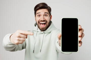 Young amazed fun impressed happy man wear mint hoody hold in hand use point index finger on mobile...