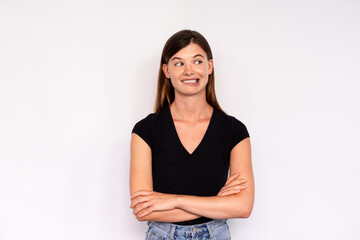 Fototapeta premium Portrait of young woman looking away and biting lip over white background. Caucasian lady wearing black T-shirt and jeans resisting laugh. Mistrust concept