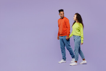 Full body side view young couple two friends family man woman of African American ethnicity wear casual clothes hold hands walk go strolling together isolated on pastel plain light purple background.