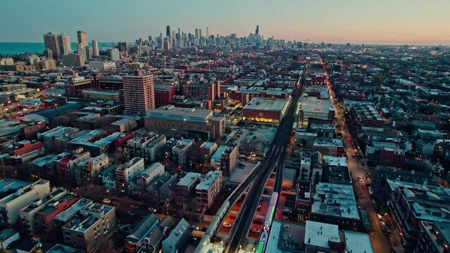 following cta holiday train decorated in chistmas on Brown Lane railroad and tilting up with an epic chicago skyline view at sunset 4k